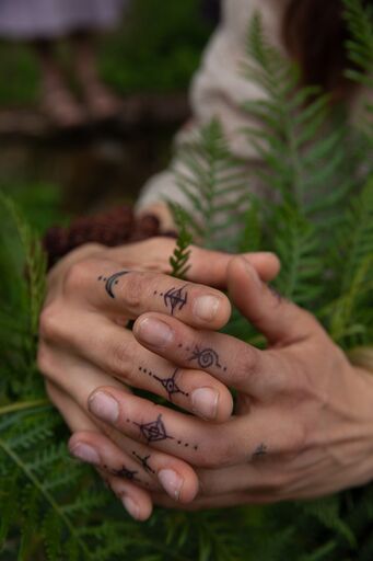 Hands covered in hand-drawn symbols resting among ferns